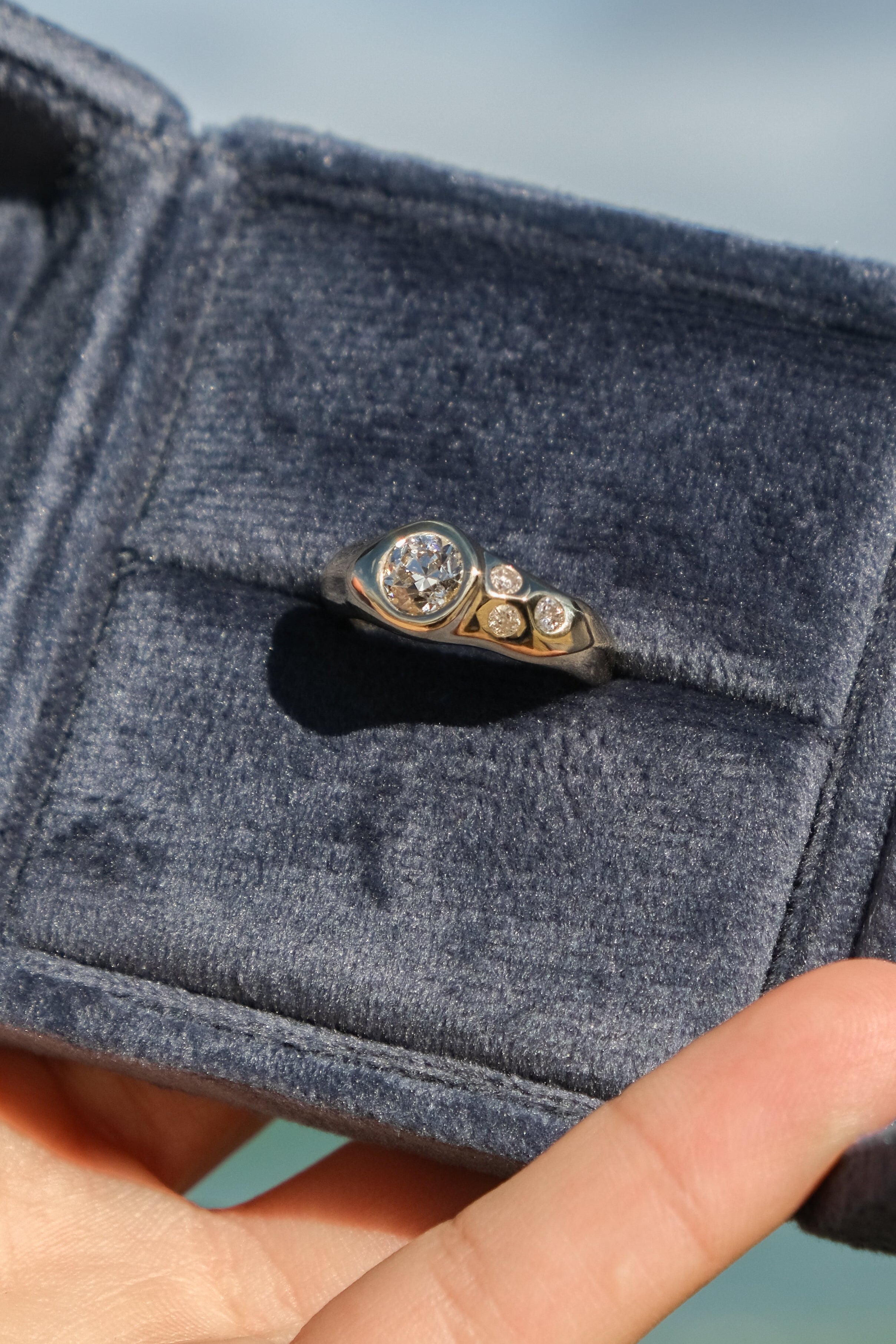 Diamond ring in a blue velvet box held by a hand with a blurred outdoor background